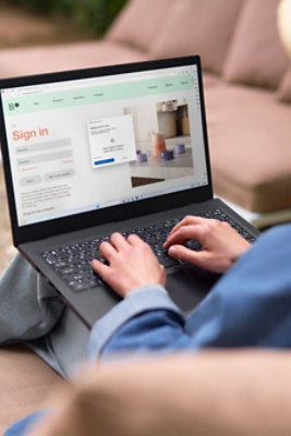 Dalam suasana santai, seseorang sedang mengetik menggunakan laptop, yang menampilkan halaman masuk dan pemberitahuan pop-up.