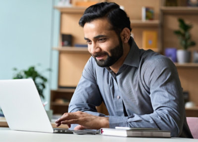 Un homme avec une barbe travaillant sur un ordinateur portable à un bureau.