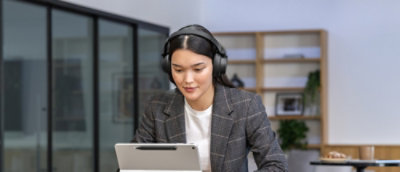 ヘッドホンを装着してノート PC を見ている女性。