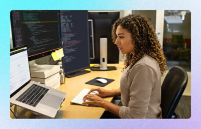 Person coding at a workstation with dual monitors and laptop.