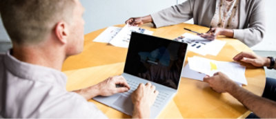 Trois personnes participant à une réunion d’affaires avec des documents et un ordinateur portable sur une table.