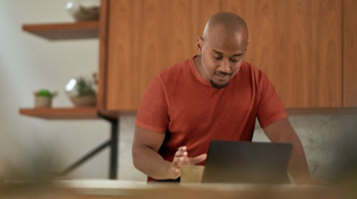 A person reaching for a coffee mug and using a laptop in their kitchen