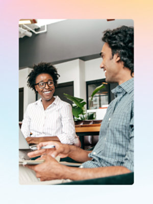 Two people sit at a desk, engaged in a conversation.