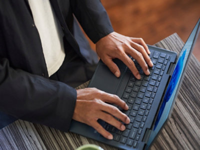 Eine Person im Business-Anzug tippt auf einer Laptop-Tastatur