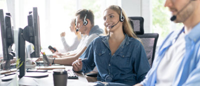 A diverse group of people working together in a busy call center, each at their own workstation with headsets.