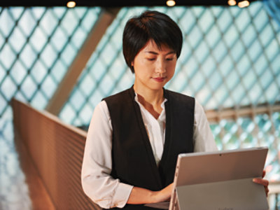 A person with short hair, wearing a white shirt and black vest, looking at a tablet.