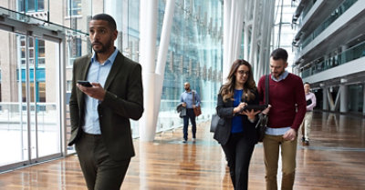 Personnes traversant un atrium vitré d’un grand bâtiment moderne. L’une d’elles utilise un appareil mobile, tandis que l’autre utilise une tablette.
