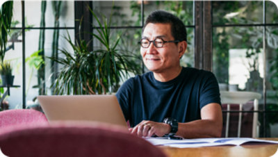 Pessoa usando óculos e uma camisa preta está sentada à mesa, sorrindo enquanto olha para um notebook. 