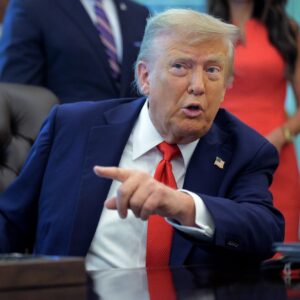 President Donald Trump sits at his desk and talks while pointing a finger.