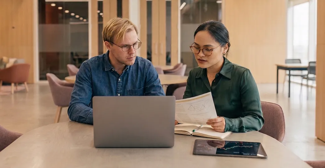 Two professionals review documents and a laptop screen in an office with a risk management flowchart overlay.