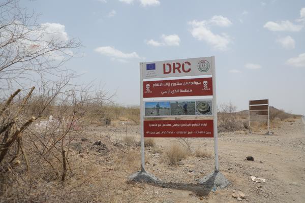 A project signboard with DRC and EU logos in a barren area warns of dangerous landmines