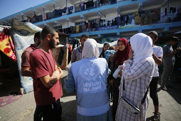 A group of people, with one person wearing a vest with UNRWA written on it, standing outside a building
