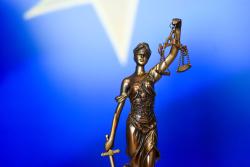 Statue of Lady Justice holding a sword and scales. Part of EU flag on background.