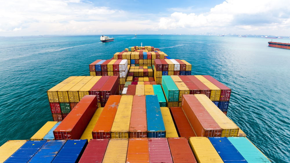 Large cargo ship transporting containers with other cargo ships in the sea in front of it.