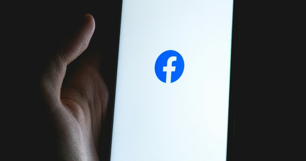 A hand holding a phone with the Facebook logo displayed on the screen