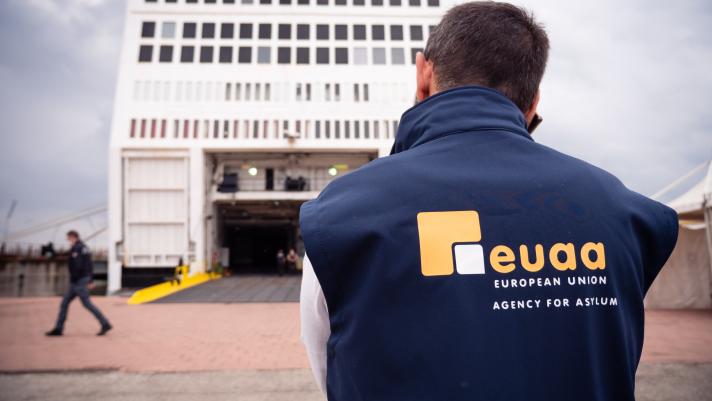An EUAA staff member is seen from the back, looking at a ferry boat which has just arrived in the port of Augusta in Sicily, while holding a phone to his ear.