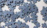 Photograph of gray jigsaw puzzle pieces scattered on a surface.