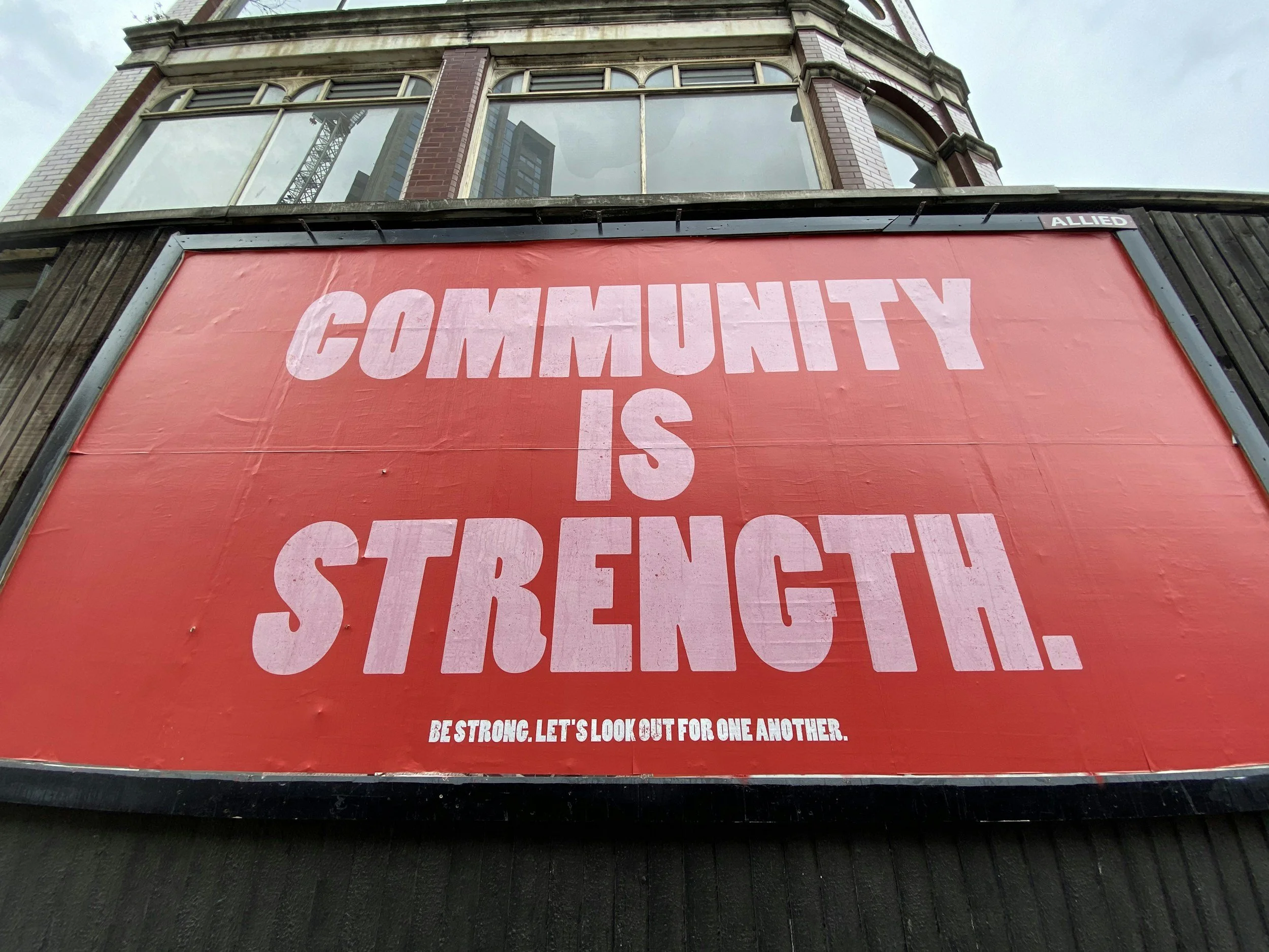 A red outdoor sign with the message 'Community is Strength.' in large white letters, and smaller text below that says 'Be strong. Let's look out for one another.'