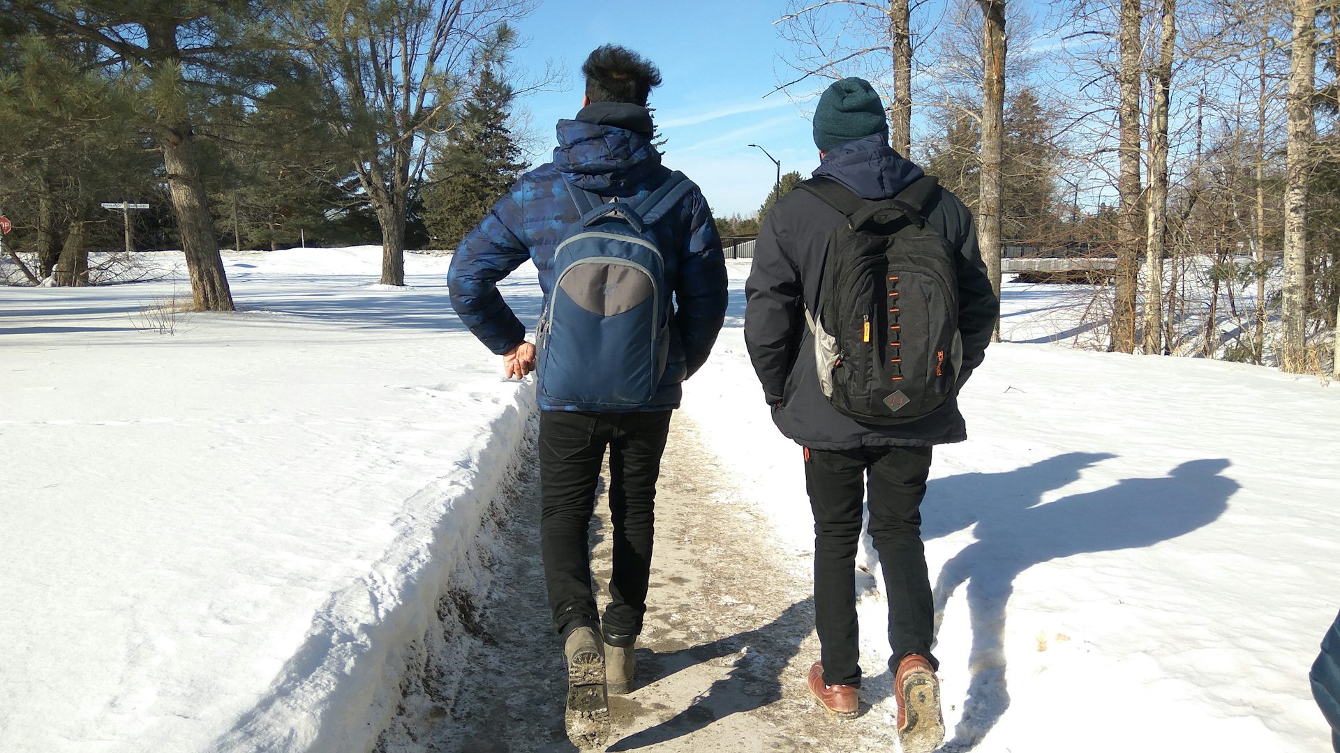 Two students seen walking in a snowy landscape on a campus.