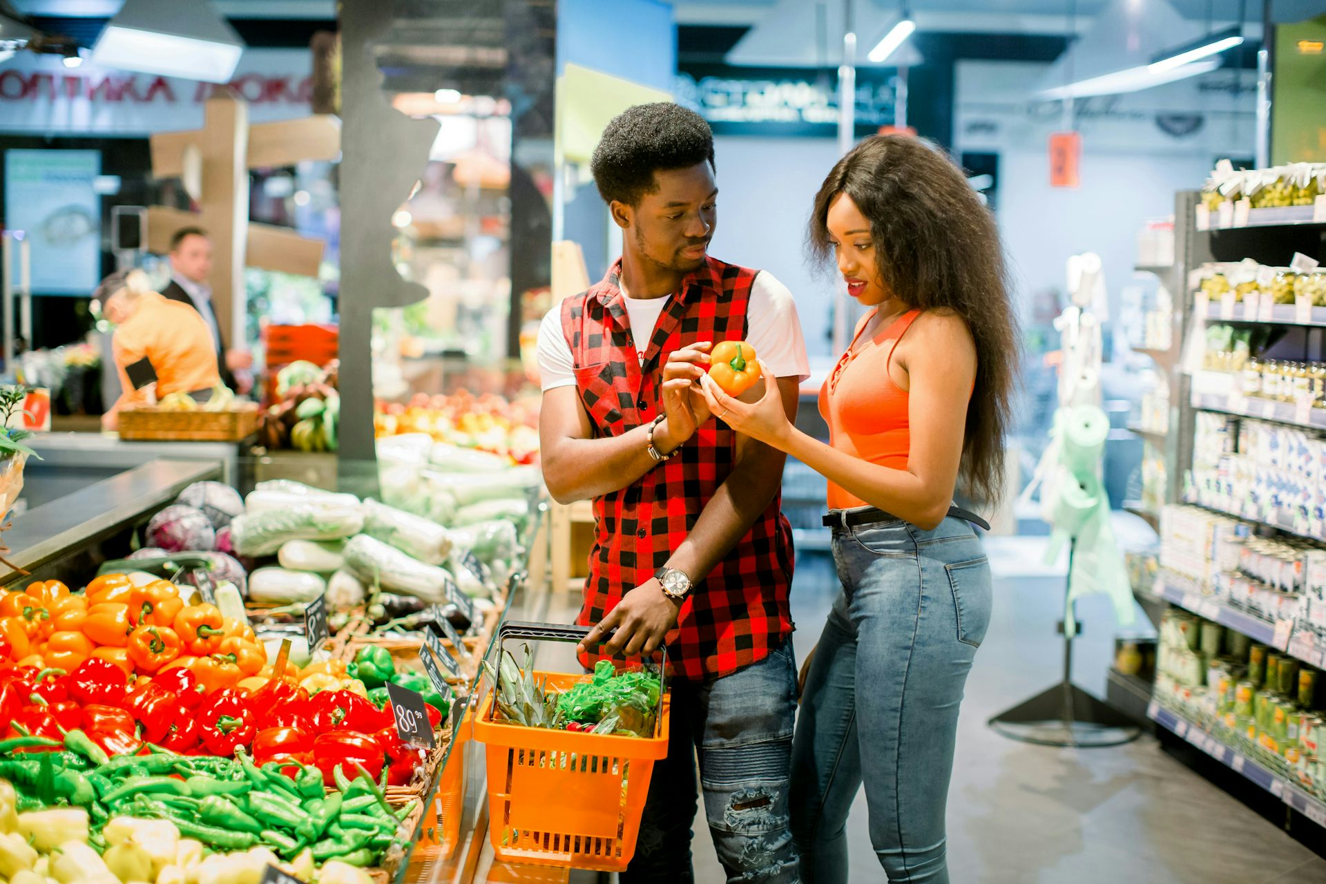 A couple looking at produce at a grocery store as they fill their shopping cart.