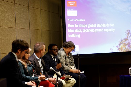 A diverse group of people seated together, focused on a large screen in front of them.