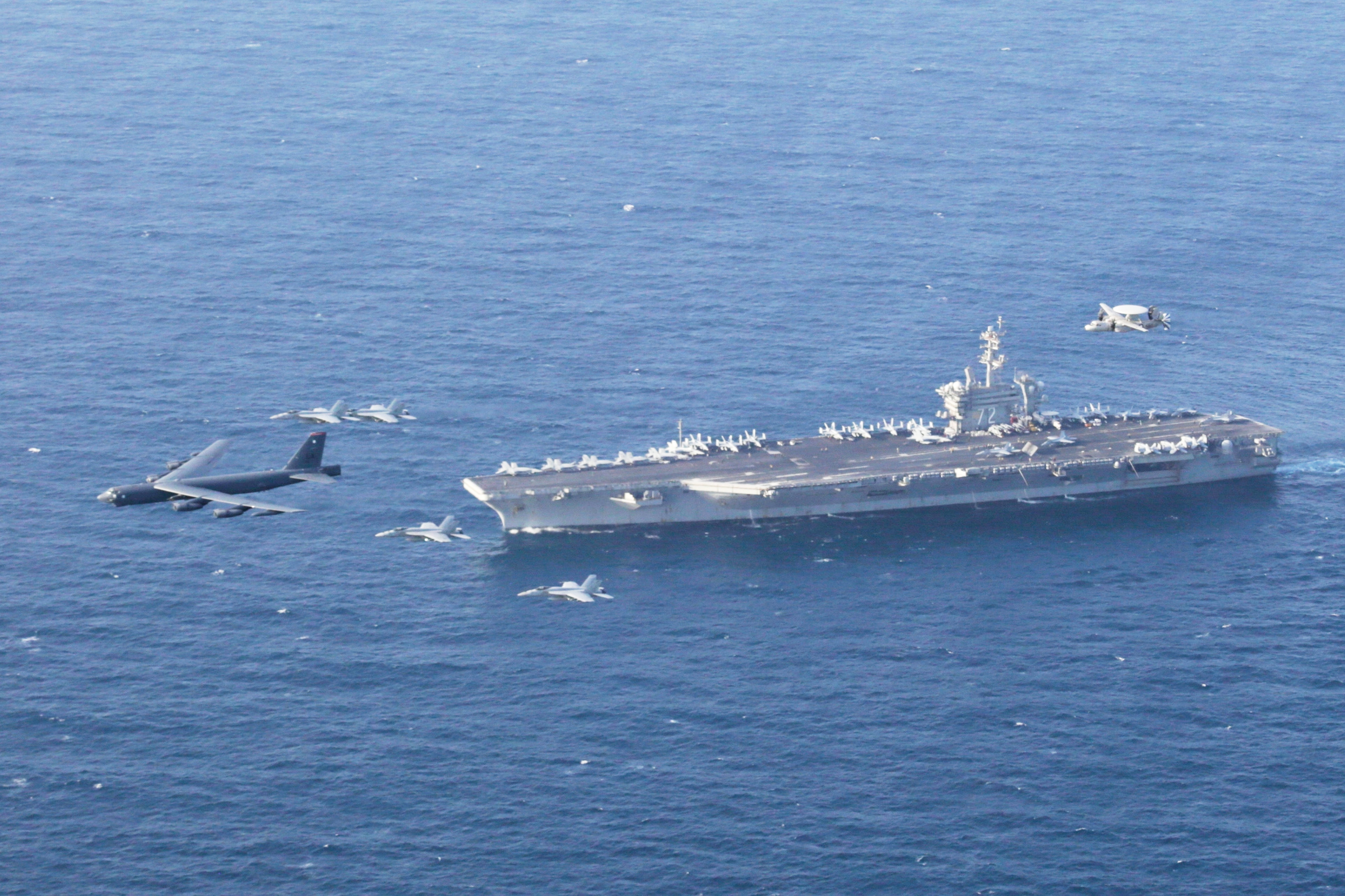 An aircraft carrier with planes flying in convoy.