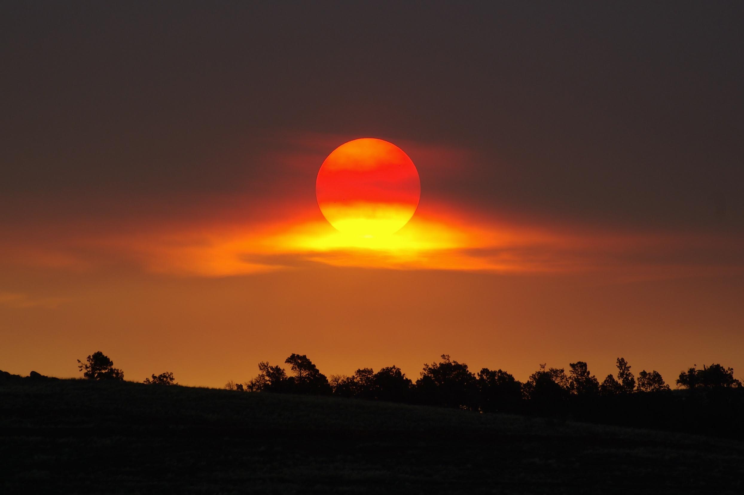 The setting sun appears through clouds.