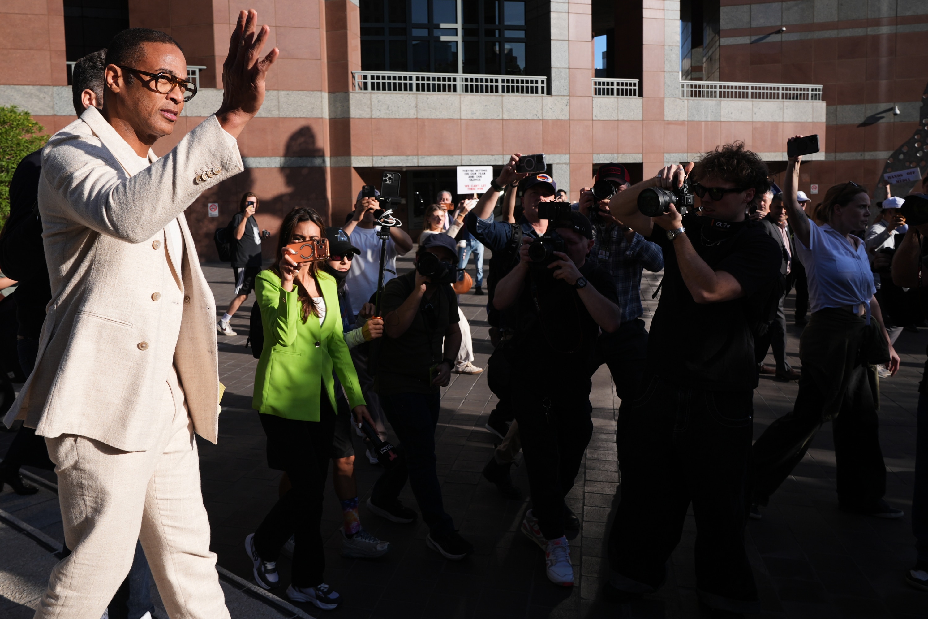 Journalist Don Lemon, dressed in a cream coloured suit, waves to reporters outside a federal building.
