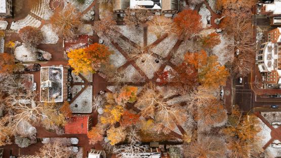 The College Green is shown with snow on the ground and colorful Fall leaves on the trees in this aerial image.