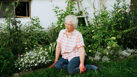 An elderly woman rests from her work in the meadow of her garden.