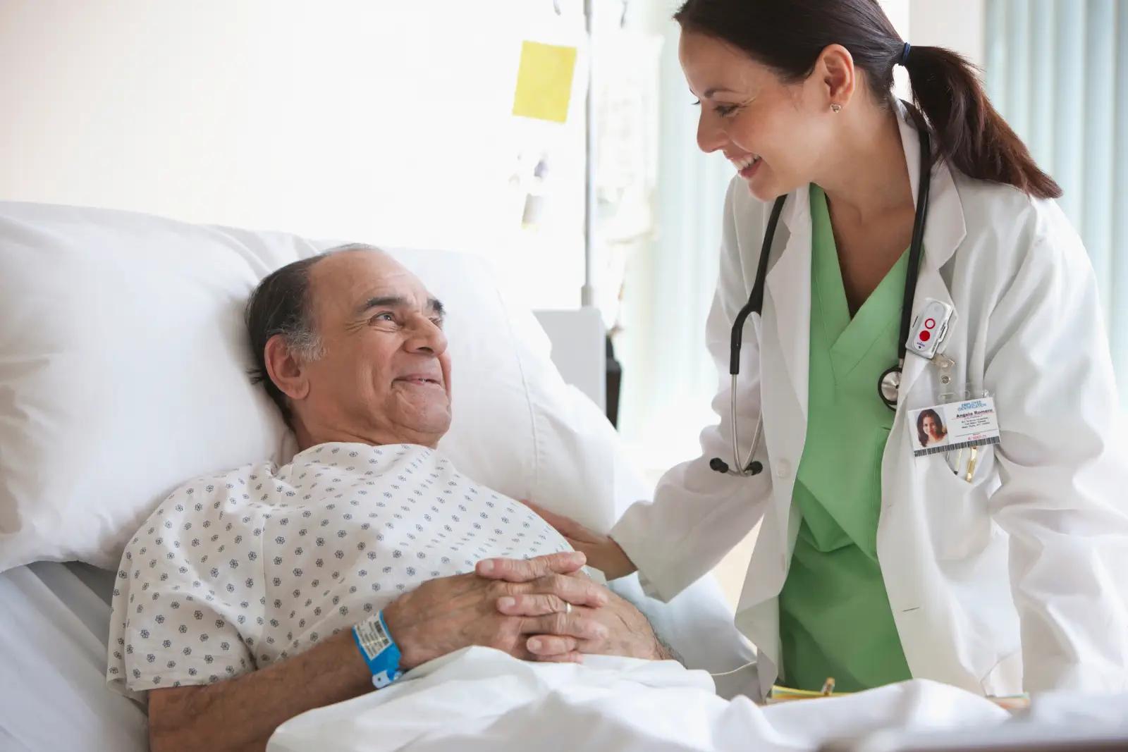 Smiling doctor reassures elderly patient in hospital bed.
