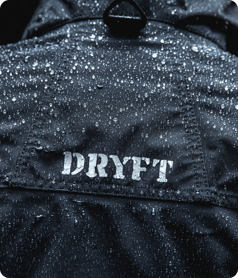 Close-up of a dark waterproof jacket covered in raindrops, with the brand “DRYFT” printed across the back.
