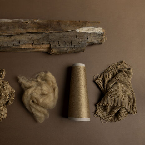 Brown-toned display of wood, pulp, fibre, thread cone and knitted fabric, showing stages from log to textile.