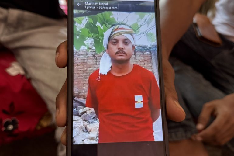 A hand holds a mobile phone with a man's picture visible on it.