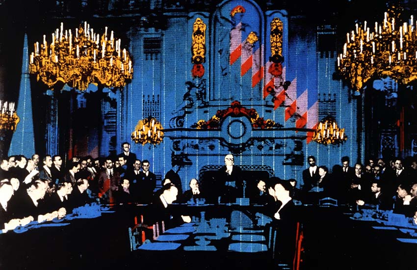 A historic meeting scene from 9 May 1950, with Robert Schuman delivering a speech and several people seated around a large table.