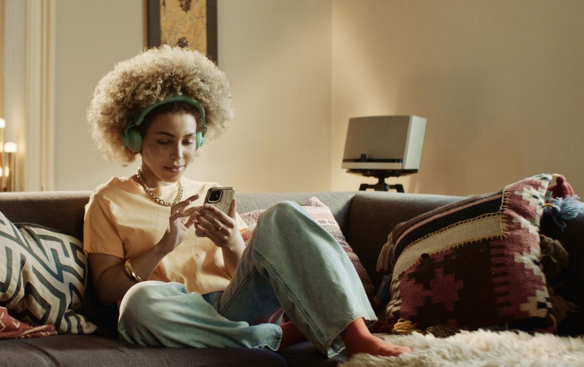 Žena sediaca na sedačke pozerajúca do svojho telefónu so schlúchadlami na ušiach