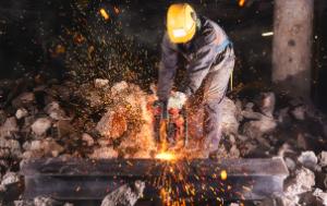 Worker with yellow helmet welding among stones, sparks flying