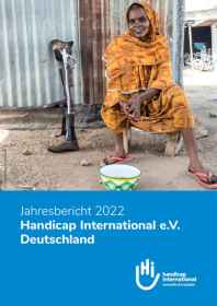 Coverbild des Jahresbericht. Eine Frau sitzt vor einem Haus. Ihre Bein Prothese lehnt an der Hauswand. Sie schaut lächelnd in die Kamera.