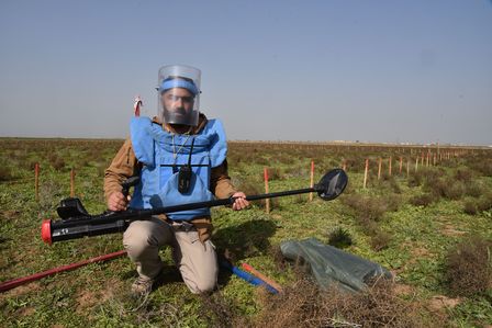 Ein Entminer in Ausrüstung kniet auf einer Wiese