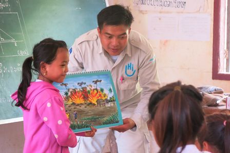 Ein Mann erklärt zwei Mädchen anhand eines Bildes die Gefahren von Blindgängern