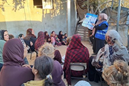 Eine HI-Expertin erklärt einer Gruppe Frauen in einem Flüchtlingscamp, woran Blindgänger zu erkennen sind. Zur Veranschaulichung hat sie ein Plakat dabei.