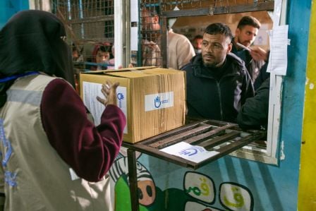 Eine HI-Mitarbeiterin überreicht dem Bewohner eines Flüchtlingscamps ein Hilfepaket.