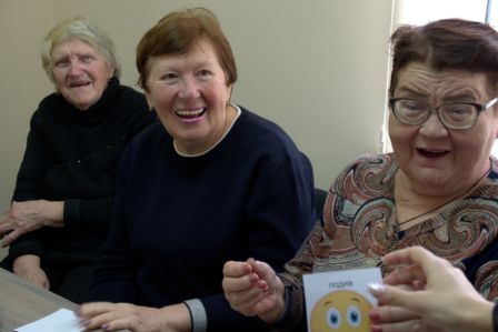 Nahaufnahme von lachenden älteren Frauen im Vordergrund ist angeschnitten eine kleine Karte mit einem Smiley zu sehen.