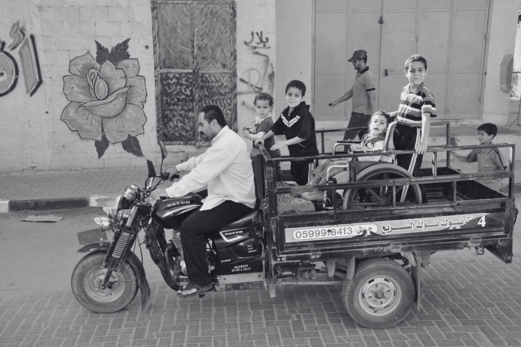 Ein kleiner Junge in einem Rollstuhl wird in einem Tuktuk gefahren. Seine Familie fährt mit ihm auf der Ladefläche.