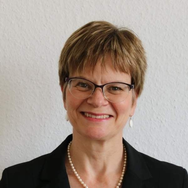 Eine Frau mit kurzen Haaren und Brille lächelt. 