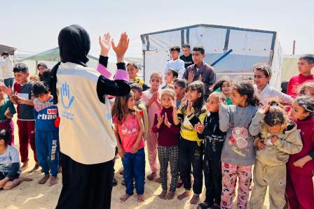 Eine HI-Mitarbeiterin klatschend vor einer Gruppe Kinder