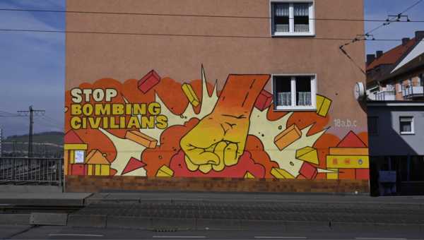 Ein Graffiti als Teil der HI Stop Bombin Civilians Kampagne. Auf dem Graffiti ist neben dem Logo und dem Claim der Kampagne auch eine Hand zu sehen, die eine Stadt aus Bauklötzen zerstört.