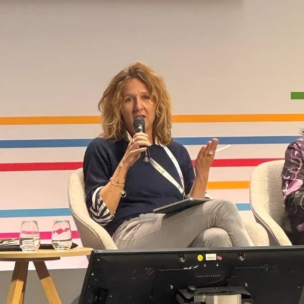 Eine blonde Frau sitzt auf einem Stuhl und spricht in ein Mikrofon. 