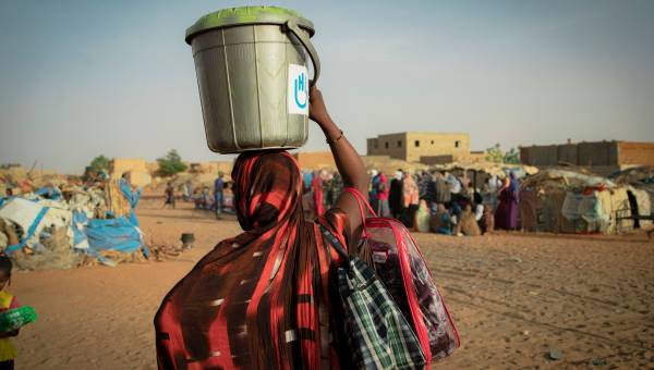 Mehrere Männer in Schutzkleidung entminen eine sandige Fläche.