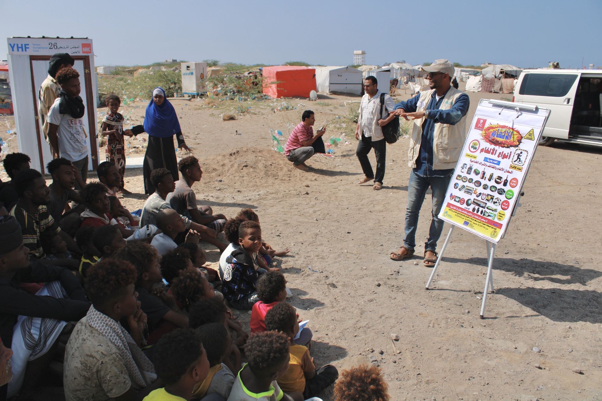 Ein HI-Mitarbeiter erklärt einer Gruppe Menschen anhand von Infotafeln, wie sie sich vor Blindgängern schützen können.
